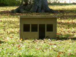 Skulptur von einem Schrebergarten-Bungalow aus Beton in kleinem Format. Die Skluptur steht auf der Wiese.