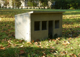 Skulptur von einem Schrebergarten-Bungalow aus Beton in kleinem Format. Die Skluptur steht auf der Wiese.